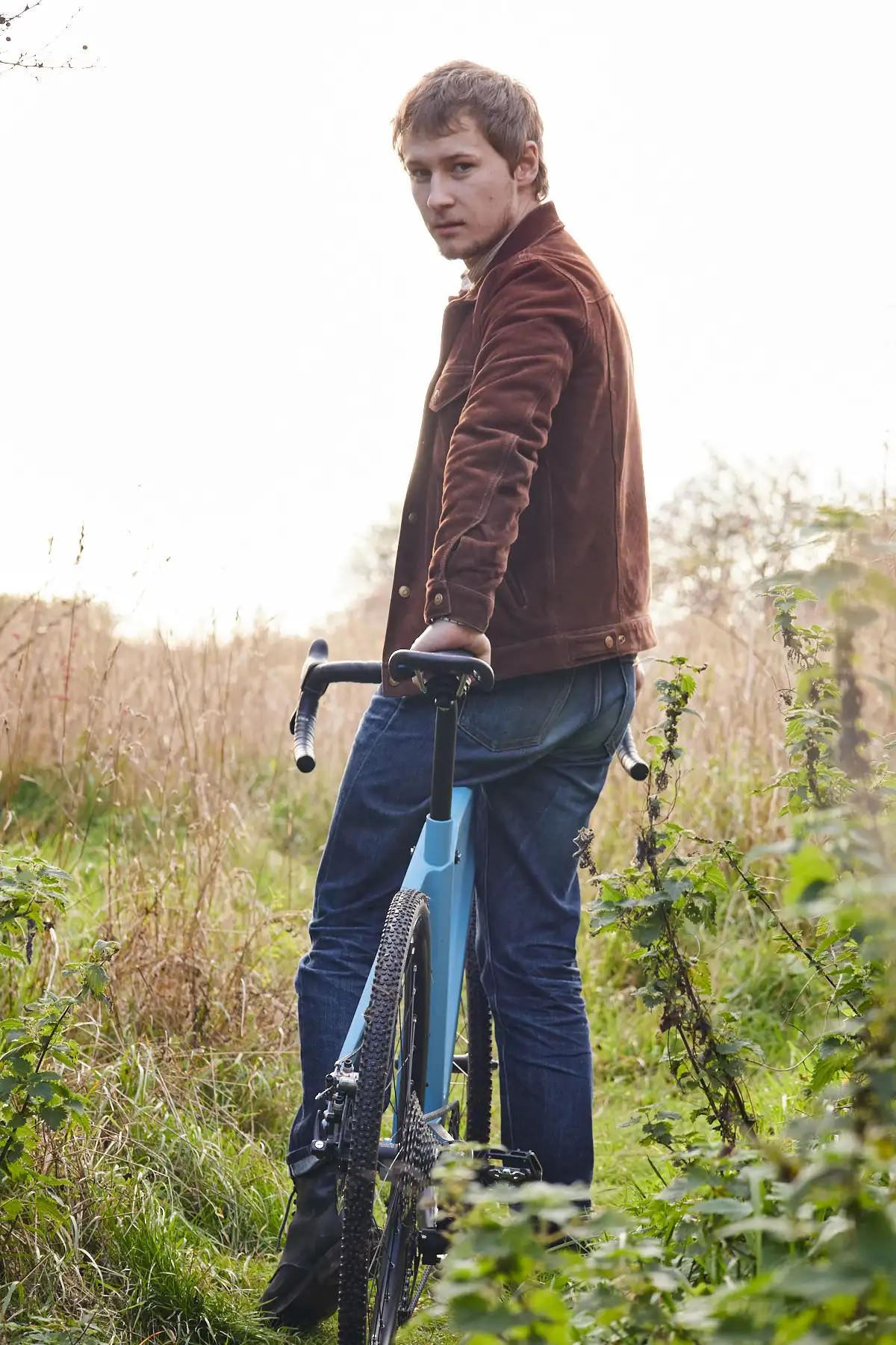 Young man looking back while relaxing on Mattis gravel bike in nature